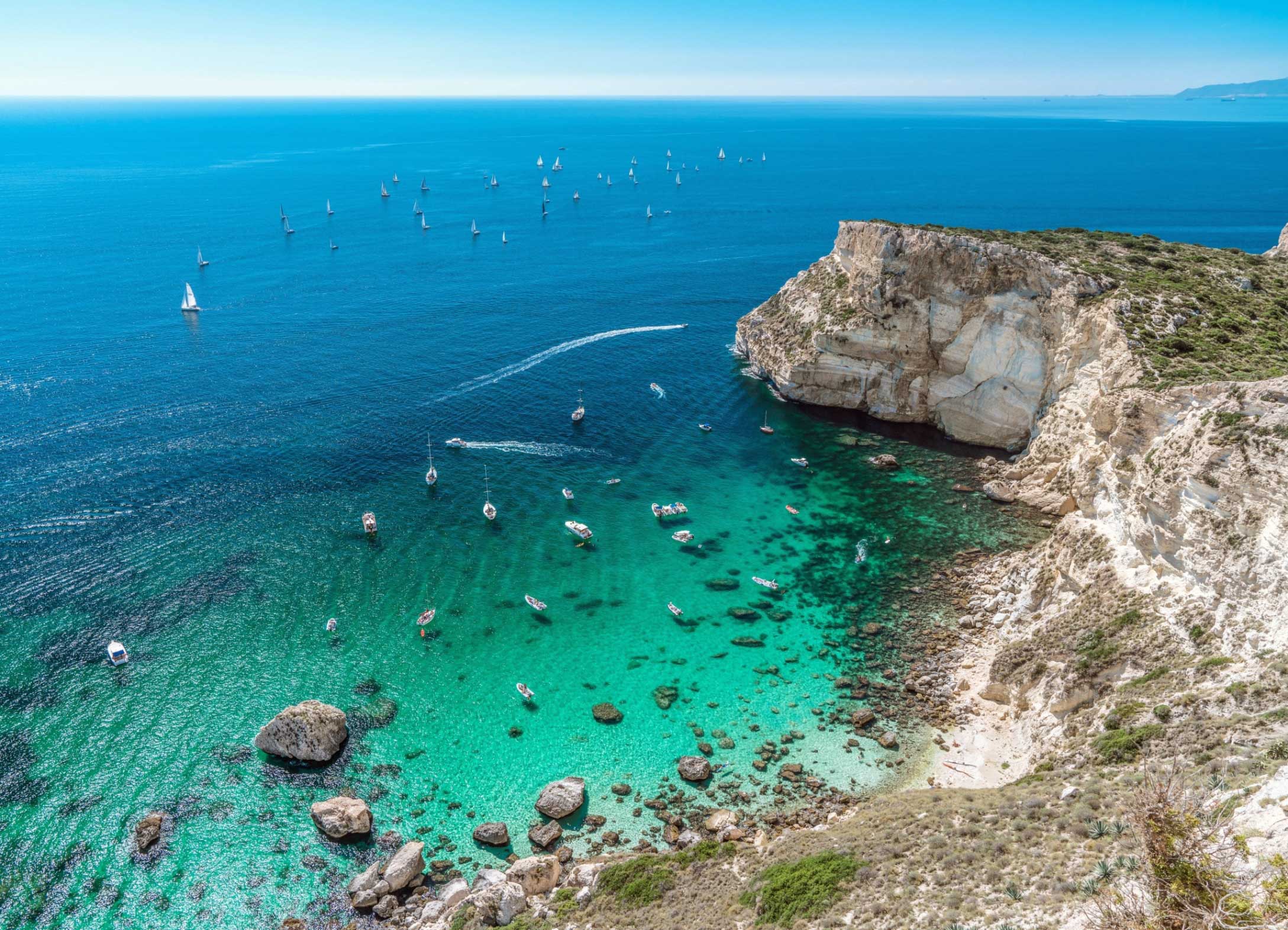 Cala Fighera dall'alto: la falesia bianca a picco e le barche sull'acqua turchese