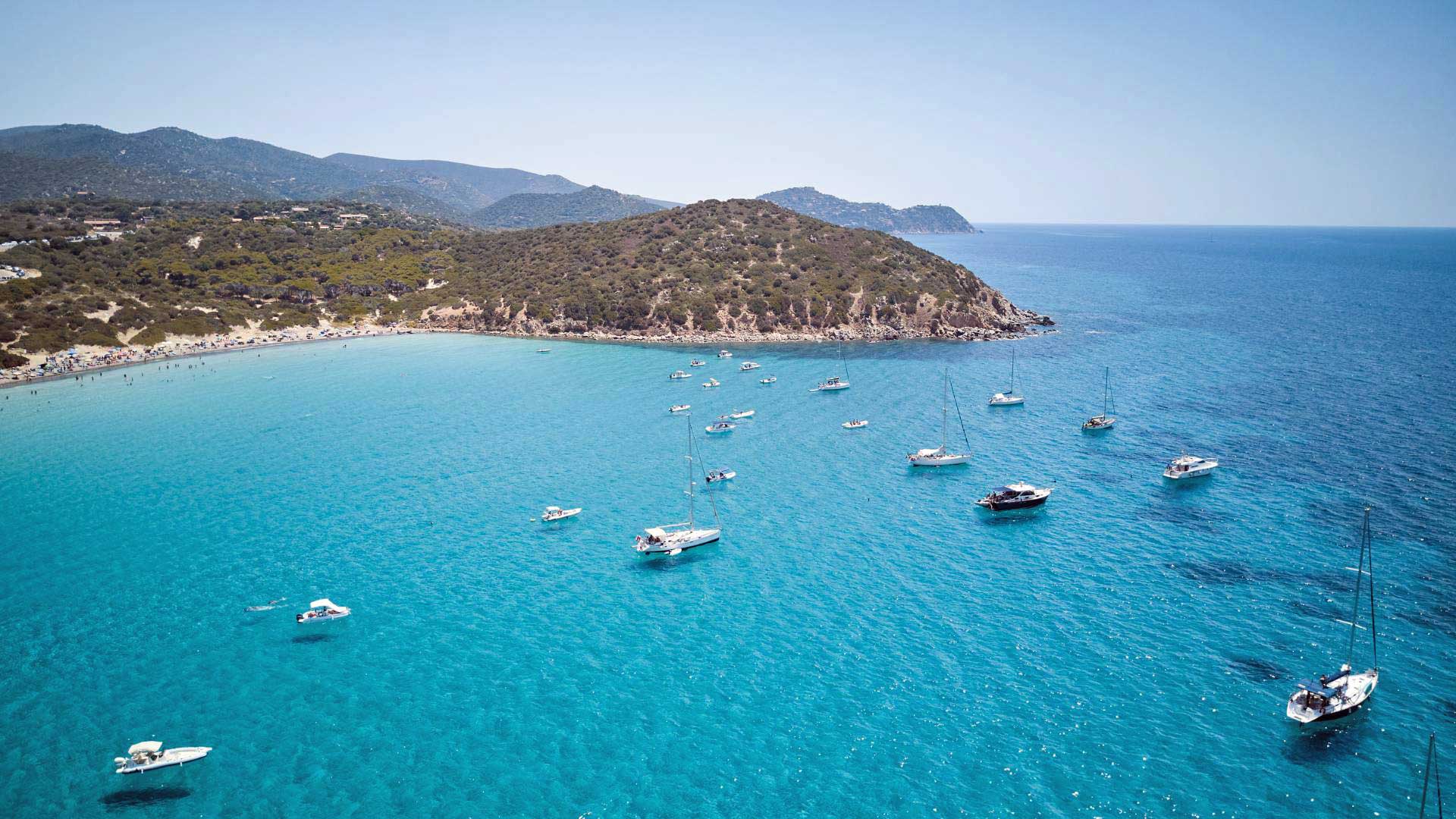 La baia di Mari Pintau vista dall'alto, con le barche all'ancora sull'acqua turchese